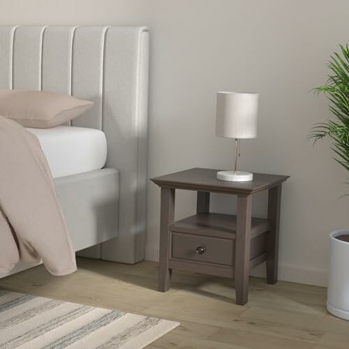 Modern bedroom with a gray nightstand, lamp, and plant.