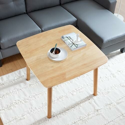 Modern wooden coffee table with books and a bowl on top, next to a gray sofa.