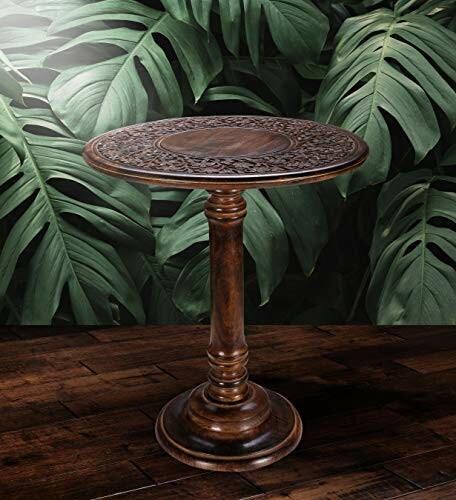 Intricately carved wooden accent table against a leafy backdrop.