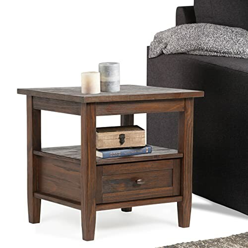 Wooden end table with candles, books, and drawer beside a sofa.