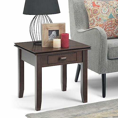 Wooden side table with a lamp, picture frame, and candles next to a sofa.